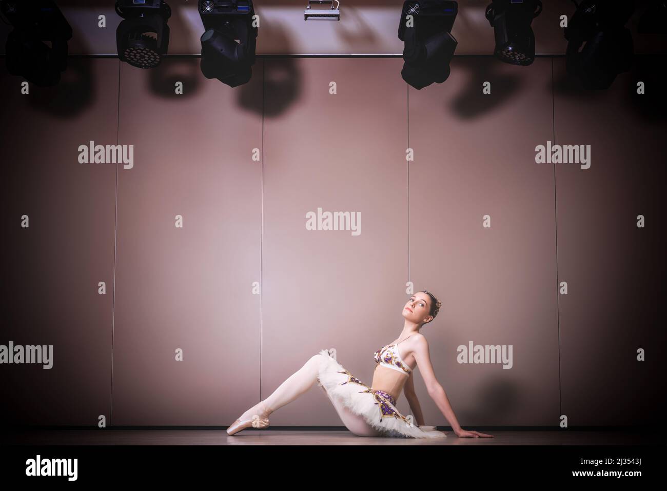 balerina joven hermosa caucásica práctica posiciones de ballet en falda tutu. Bailarín de ballet clásico sentado en el suelo del estudio Foto de stock