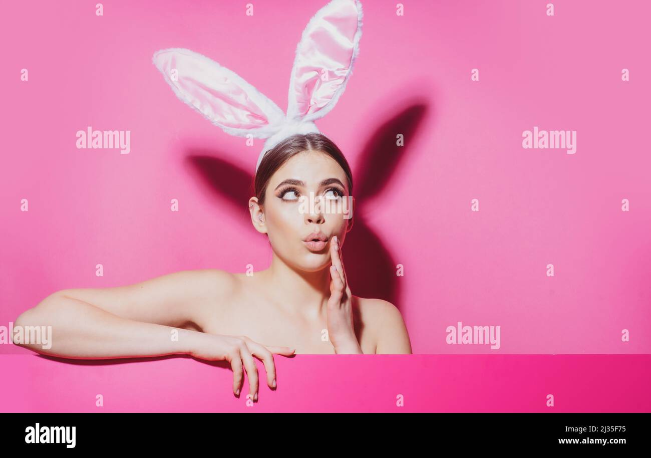 Mujer joven sorprendida con orejas de conejo aisladas en rosa. Foto de stock