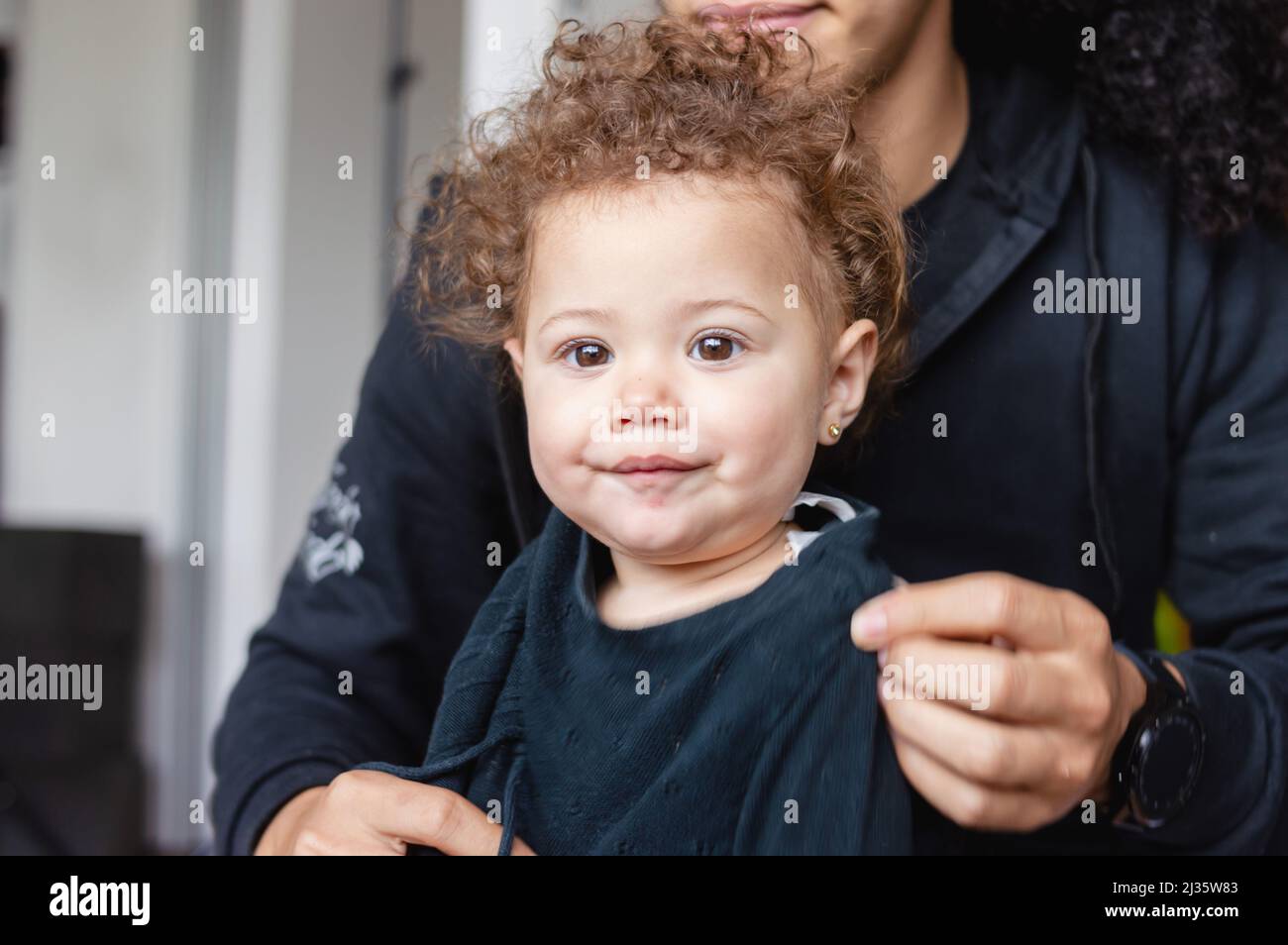 hermoso bebé caucásico con pelo rizado y pelo rojo, mirando la cámara de  pie con su papá detrás de ella en la sala de estar en casa Fotografía de  stock - Alamy