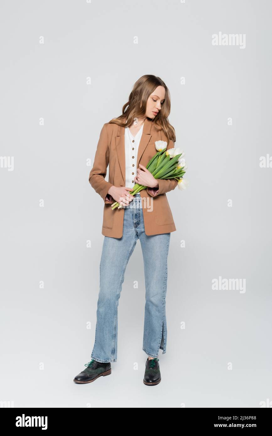 vista completa de mujer en blazer beige y jeans sosteniendo tulipanes sobre  fondo gris Fotografía de stock - Alamy