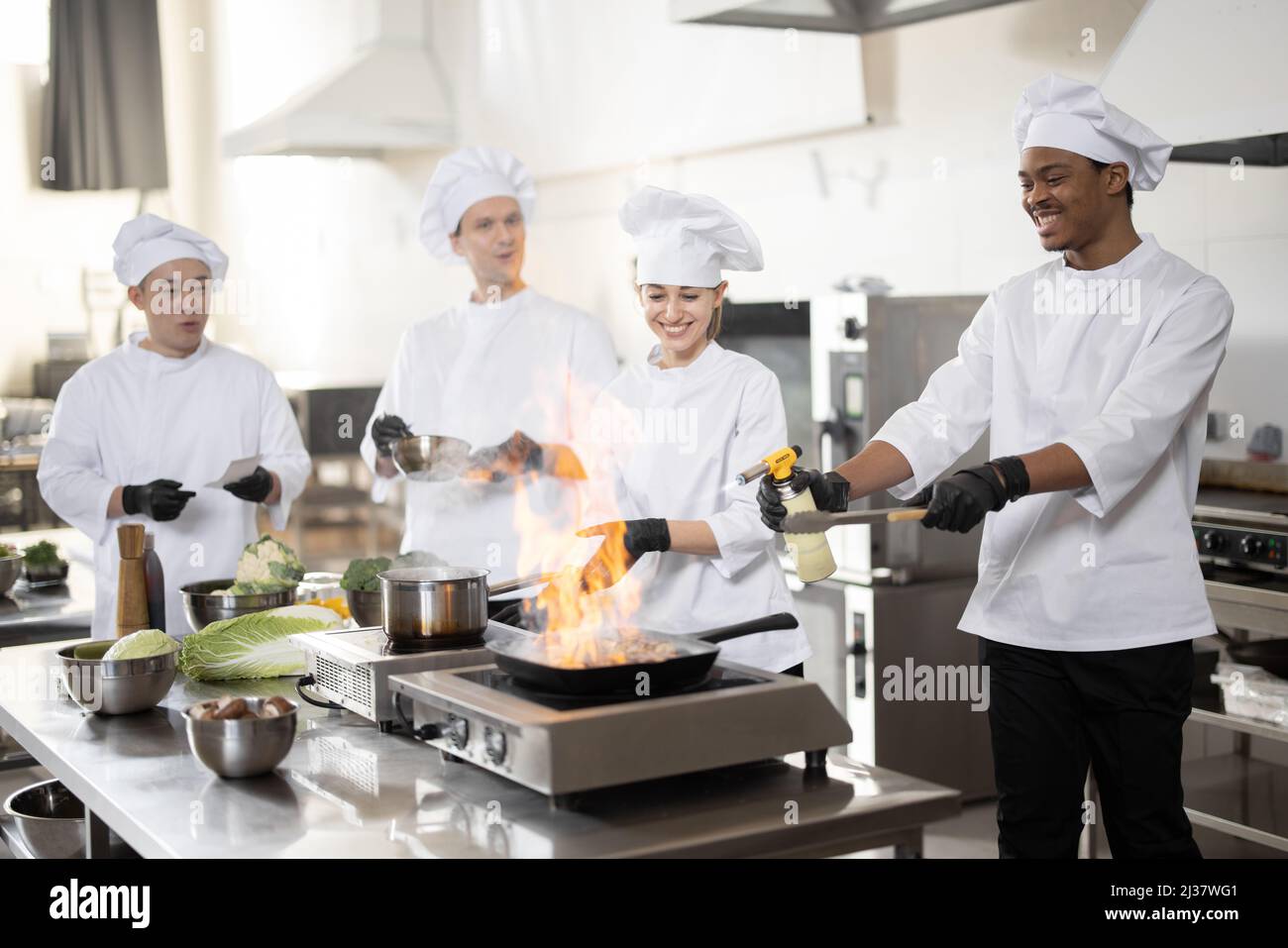 Equipo multirracial de cocineros profesionales en uniforme preparando  comidas para un restaurante en la cocina. Pan de comida latina, cocina  europea que hace salsa y chef asiático que gestiona el proceso. Trabajo