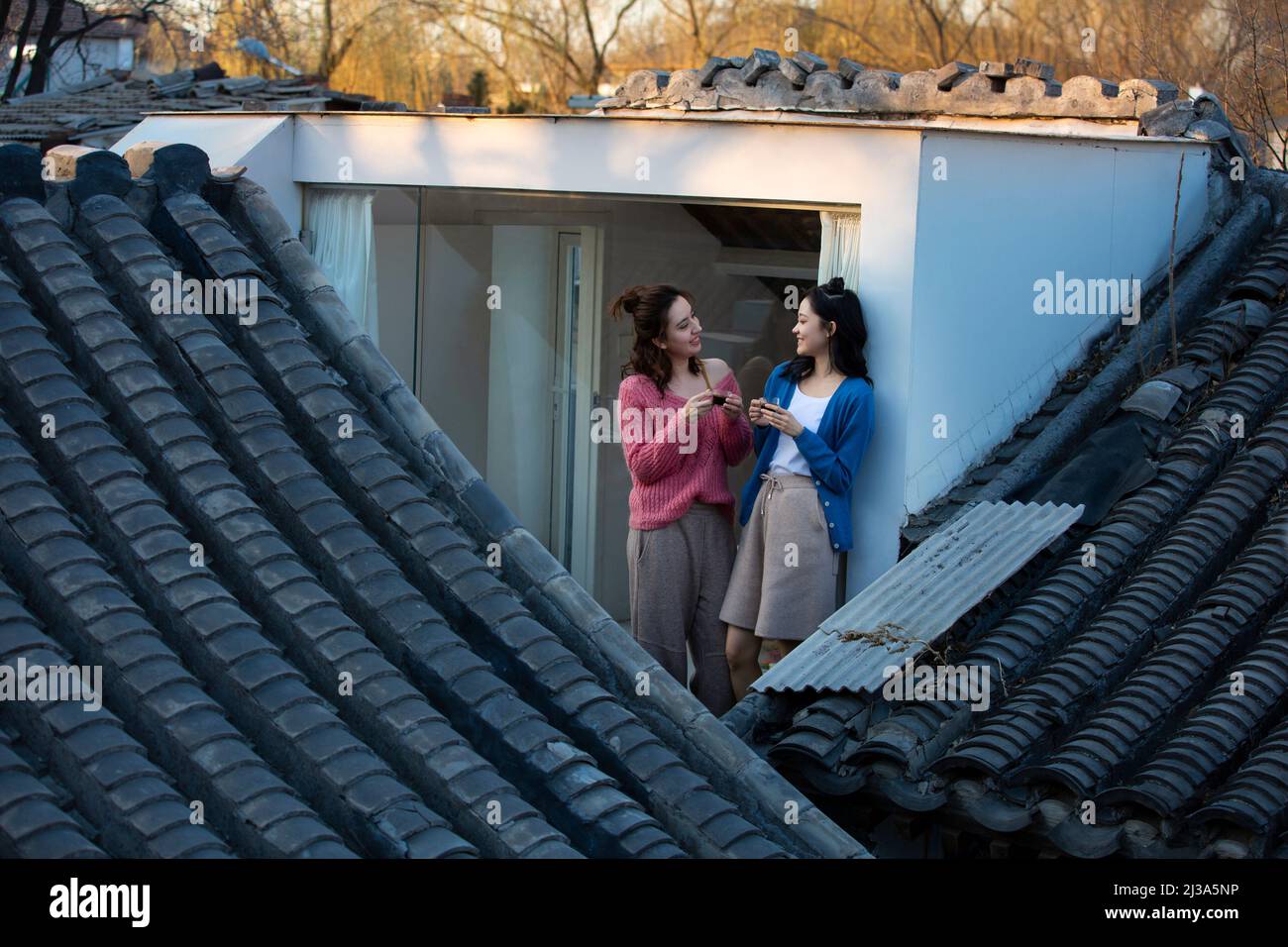 Mujeres jóvenes chinas se relajan en el techo de una casa tradicional en el patio de Beijing - foto de archivo Foto de stock