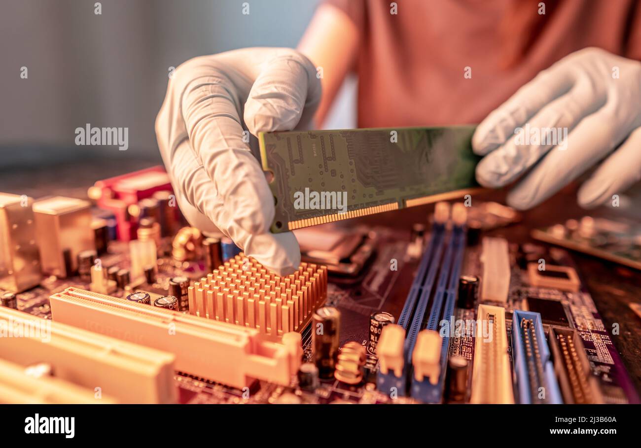 Un ingeniero de reparación sostiene un chip RAM con las en guantes negros, inserta la RAM del ordenador en el zócalo de la placa base del ordenador. La conce Fotografía de