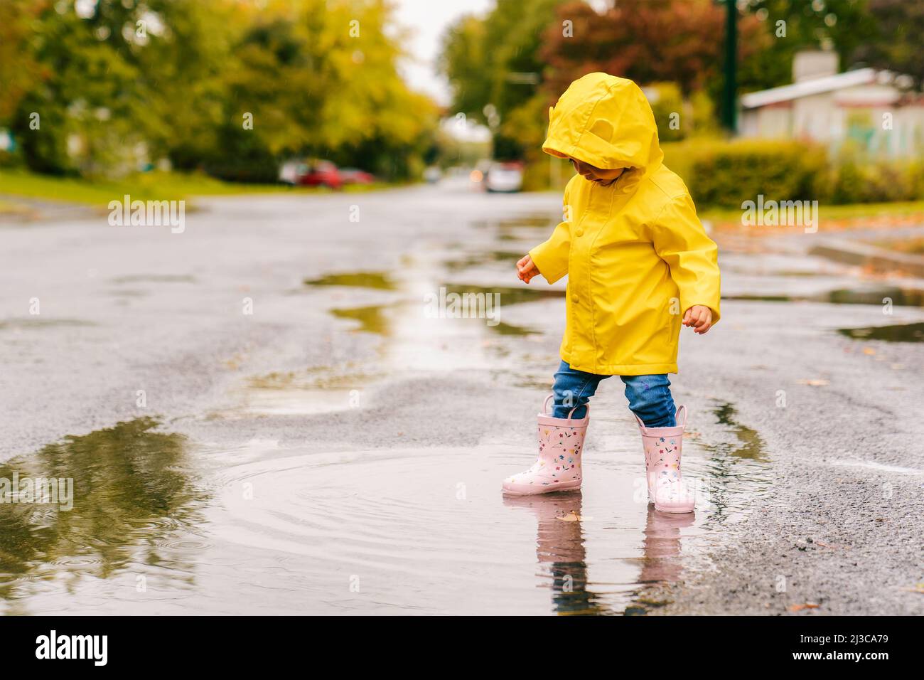 Gracioso lindo niña con abrigo amarillo impermeable y botas jugando en la lluvia Fotografía de stock - Alamy
