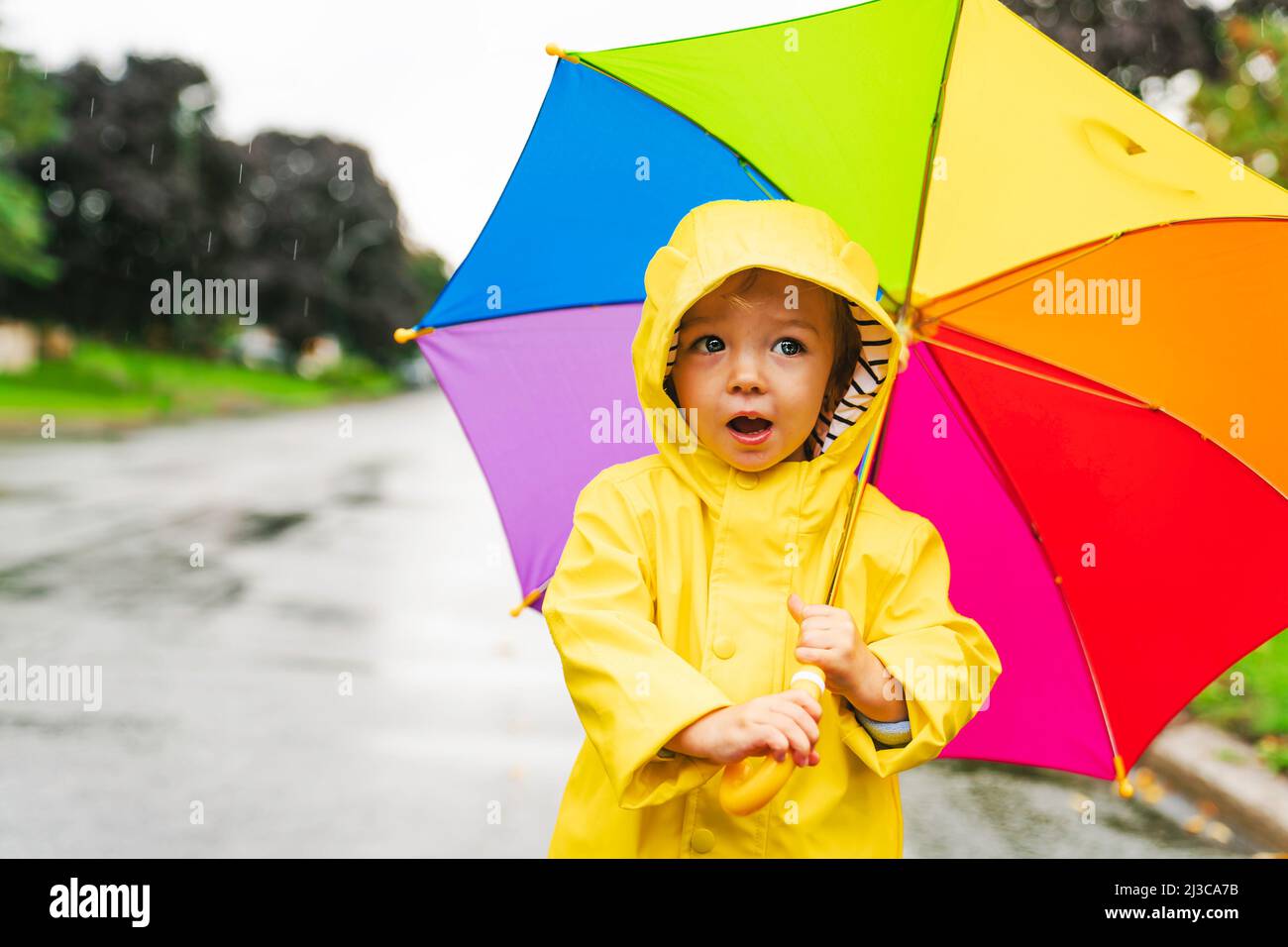 Gracioso lindo bebé niña con abrigo impermeable amarillo y botas  sosteniendo un colorido paraguas jugando bajo la lluvia Fotografía de stock  - Alamy