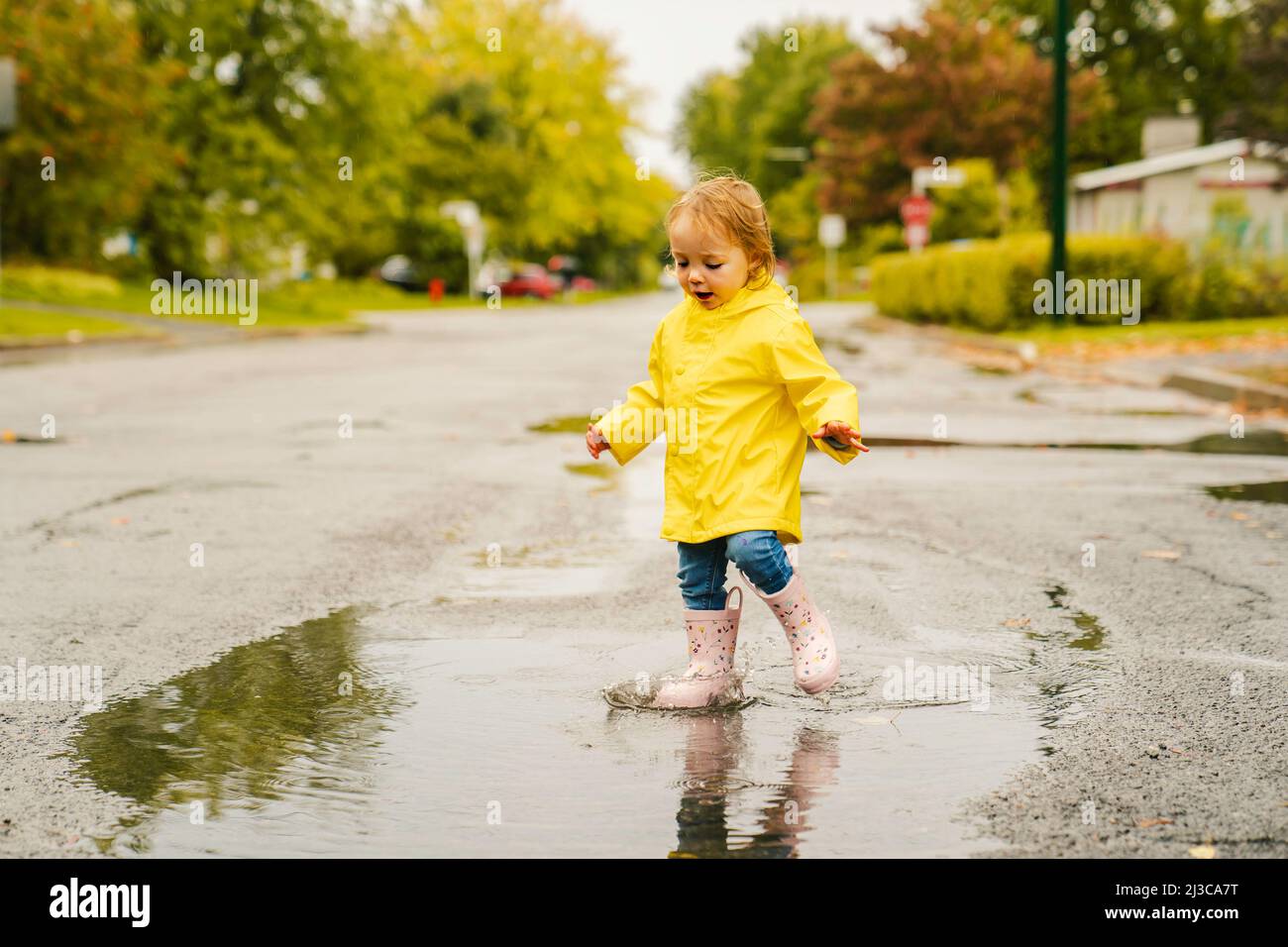 Gracioso lindo bebé niña con abrigo amarillo impermeable y botas jugando en  la lluvia Fotografía de stock - Alamy