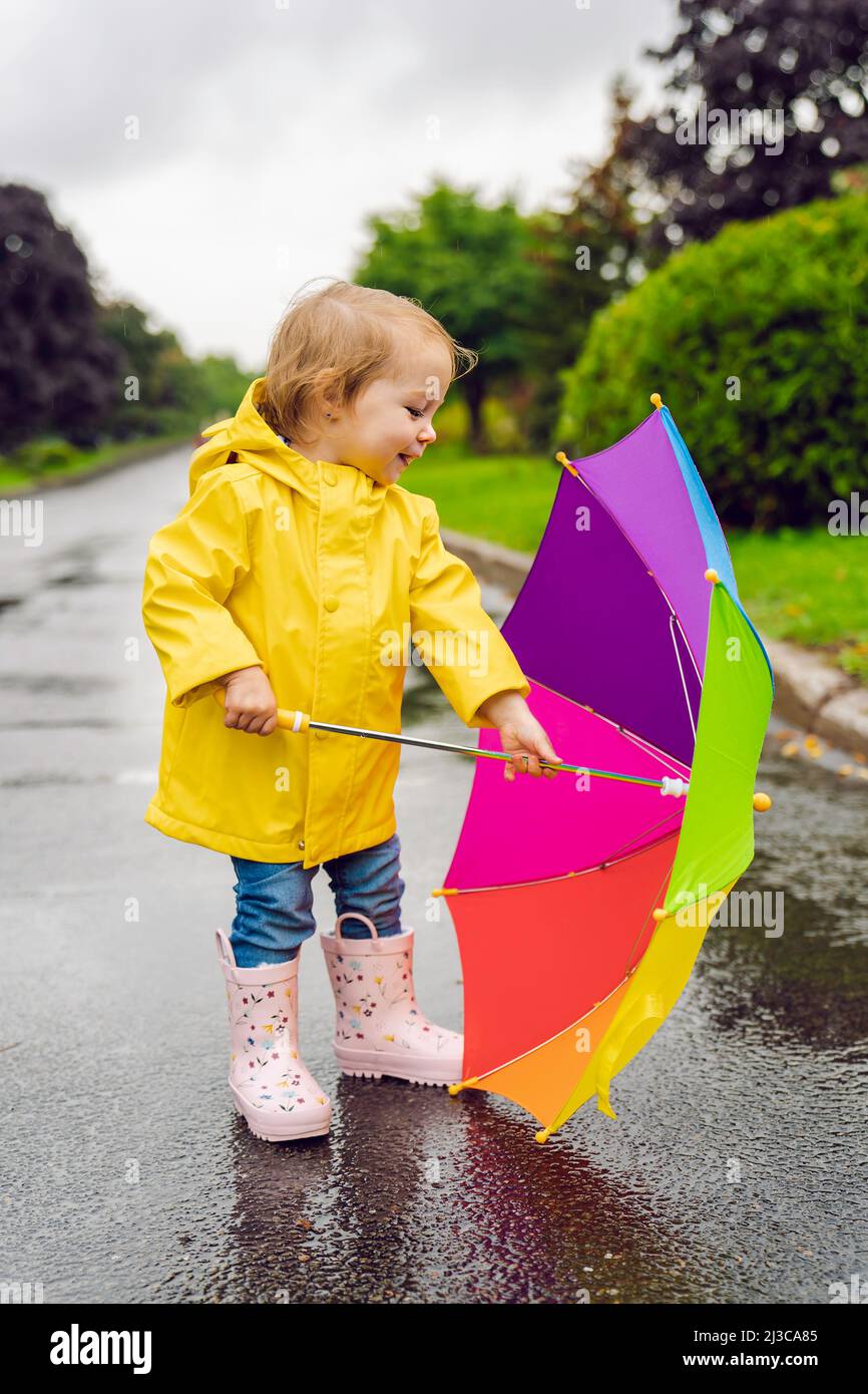 Gracioso lindo bebé niña con abrigo impermeable amarillo y botas  sosteniendo un colorido paraguas jugando bajo la lluvia Fotografía de stock  - Alamy
