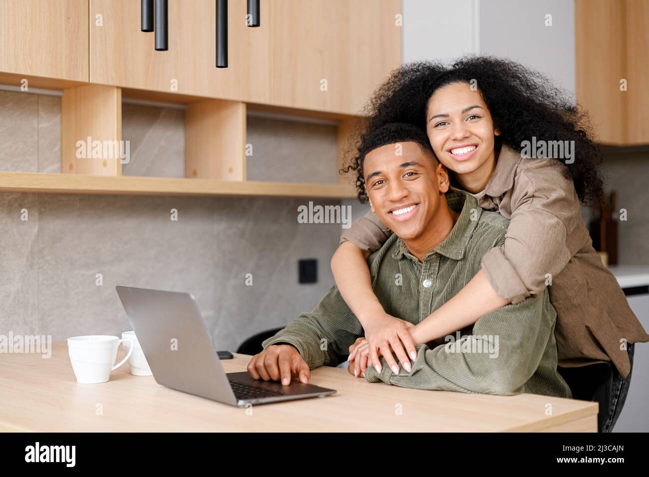 Mujer biracial abrazando al hombre desde atrás. Mezcla de etnicidad pareja relajarse en el nuevo apartamento en casa mientras navega por Internet en el ordenador portátil. Muestre el amor diario en el concepto más simple de maneras Foto de stock