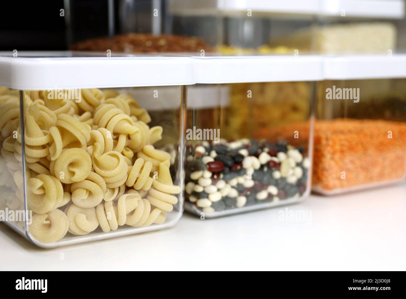 Recipientes transparentes llenos de pasta, legumbres y cereales en el estante de la cocina. Organización del almacenamiento de alimentos a granel Foto de stock