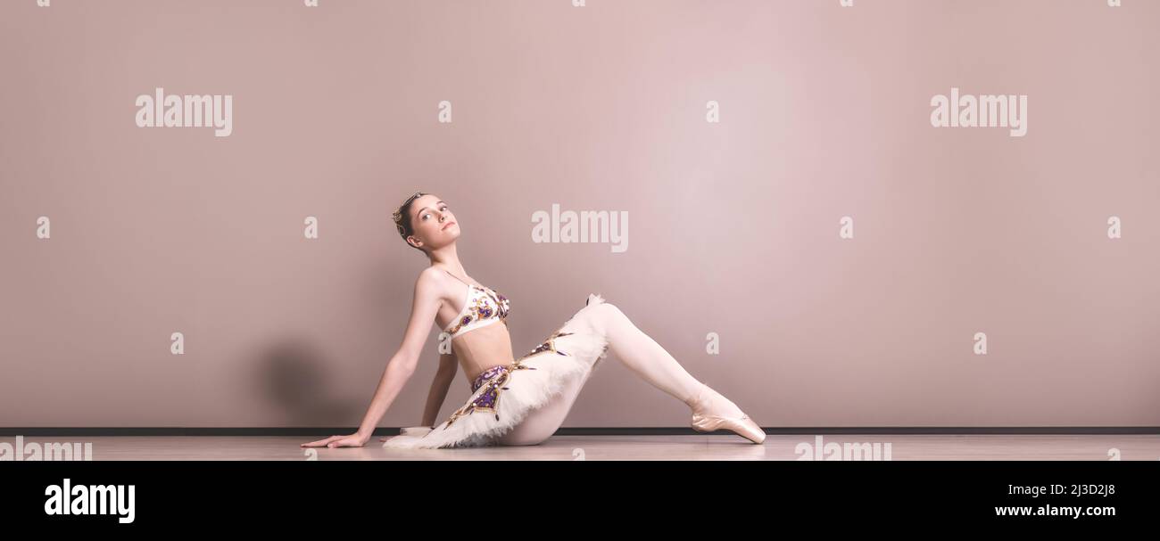 balerina joven hermosa caucásica práctica posiciones de ballet en falda tutu. Bailarín de ballet clásico sentado en el suelo del estudio Foto de stock