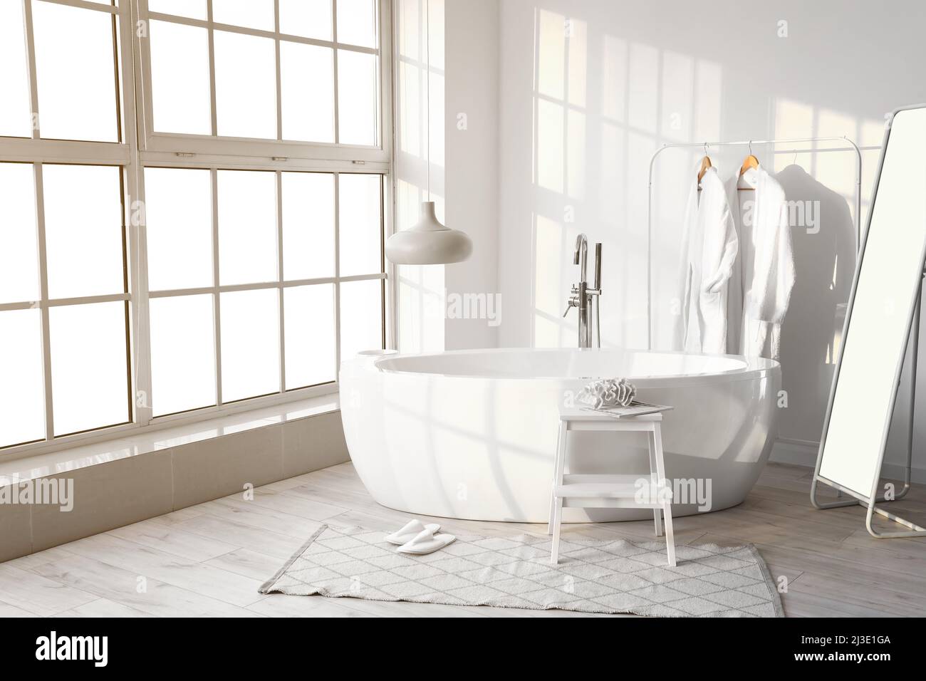Interior de un elegante baño con bañera, tendedero con albornoces