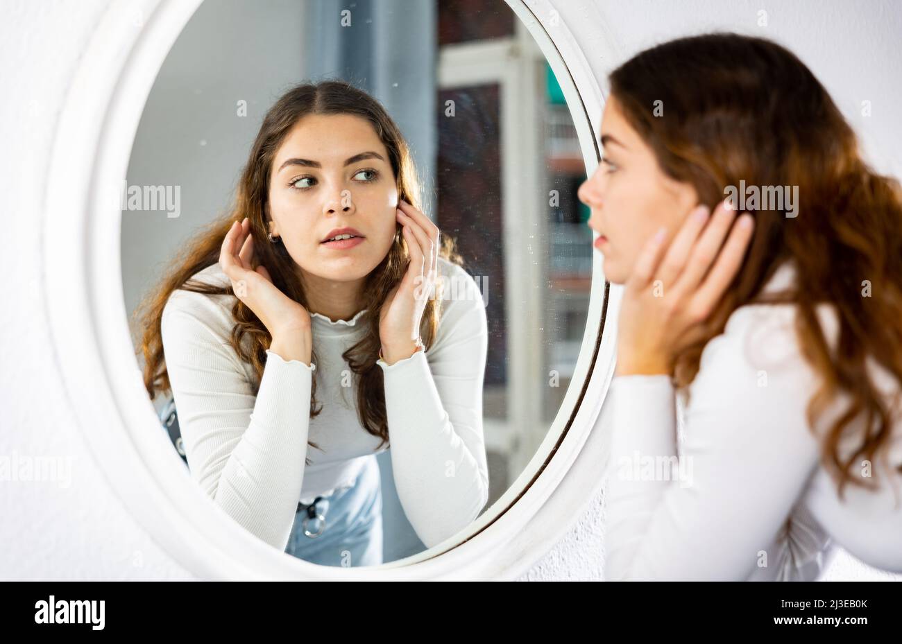 Mujer de pie frente al espejo y mirando su cara Fotografía de stock - Alamy