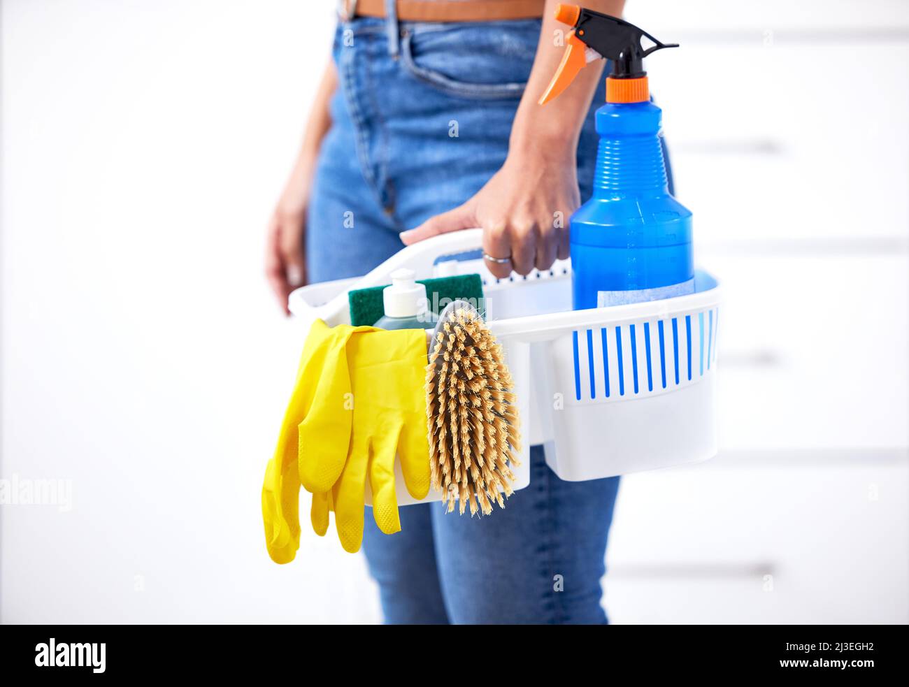 Mujer sosteniendo una cesta con productos de limpieza sobre fondo de color