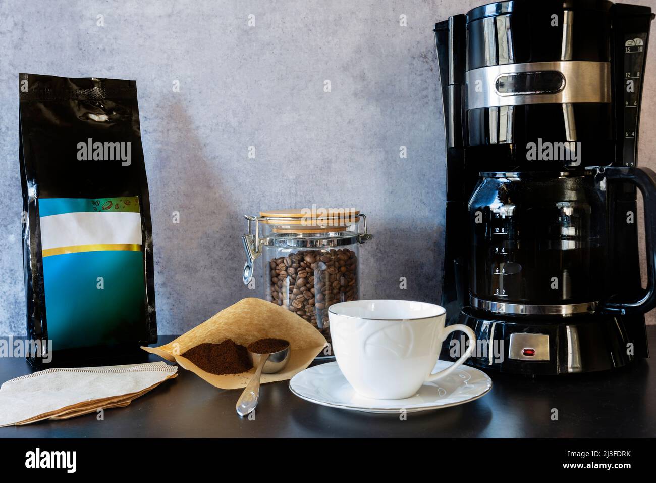 https://c8.alamy.com/compes/2j3fdrk/maquina-de-cafe-una-taza-un-tarro-lleno-de-granos-de-cafe-y-una-cuchara-de-cafe-de-filtro-una-mano-que-vierte-el-cafe-de-filtro-2j3fdrk.jpg