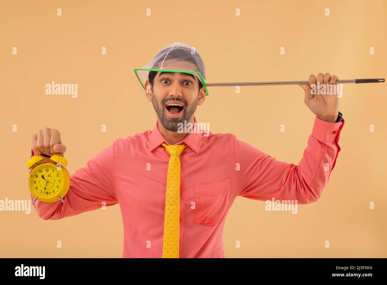 Un hombre corporativo feliz sosteniendo el reloj de alarma amarillo y la red entomológica de aterrizaje en sus manos Foto de stock