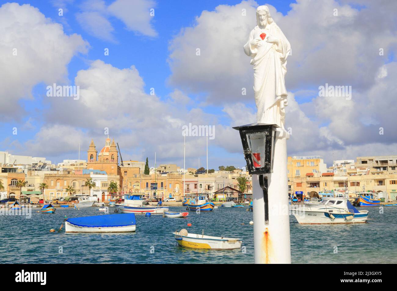 Malta, Marsaxlokk, estatua de Jesucristo con el puerto pesquero y al fondo la iglesia parroquial de Nuestra Señora de Pompeya (1897) Foto de stock