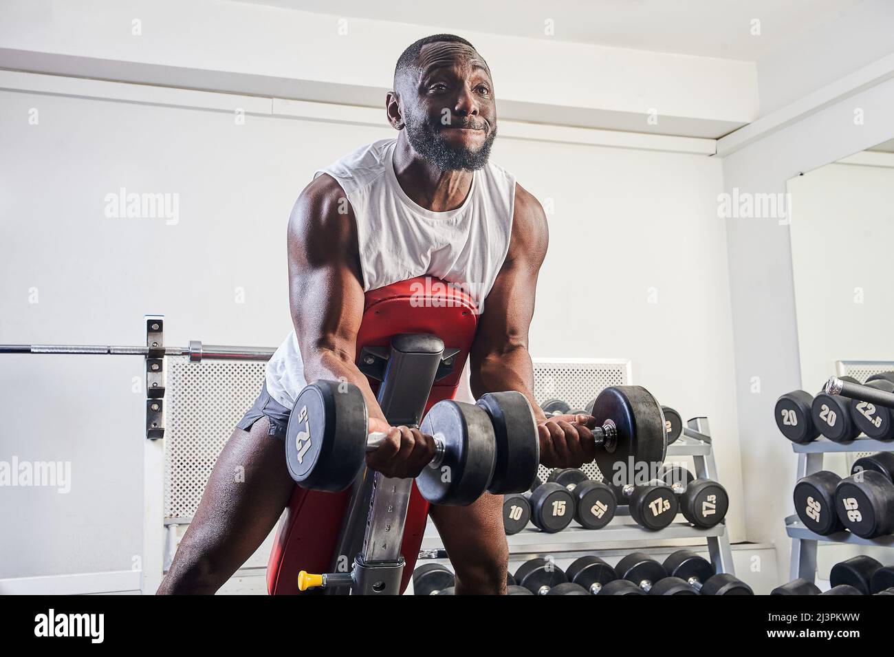 Un hombre afroamericano sacude sus bíceps en un banco inclinado en el  gimnasio Fotografía de stock - Alamy