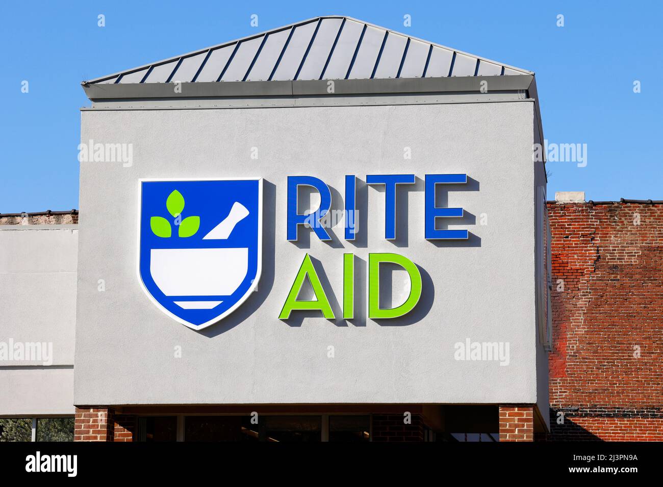 El logotipo de Rite Aid en una farmacia minorista en Filadelfia con una pared de ladrillo y soleado cielo azul en el fondo Foto de stock