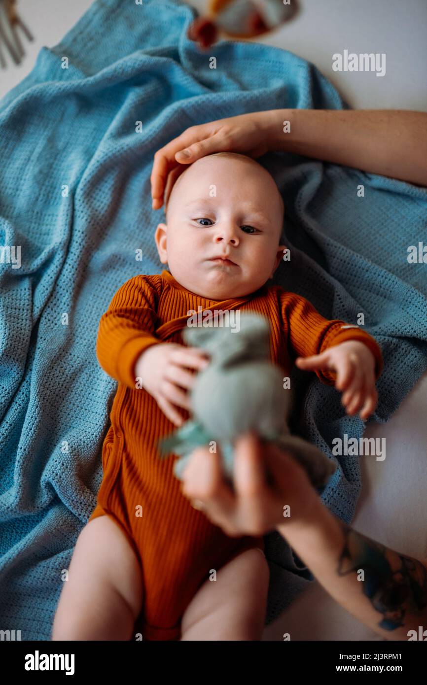 Mamá le muestra al bebé con el ojo azul un juguete y le acaricia la cabeza  Fotografía de stock - Alamy
