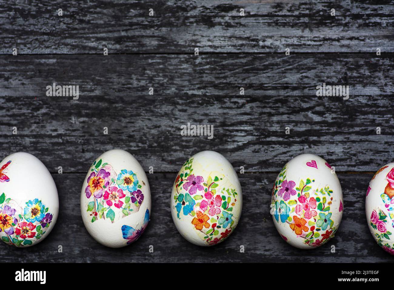 Huevos de Pascua blancos hechos con técnica de desacoplamiento con motivos florales sobre un fondo negro rústico con gran espacio de copia Foto de stock