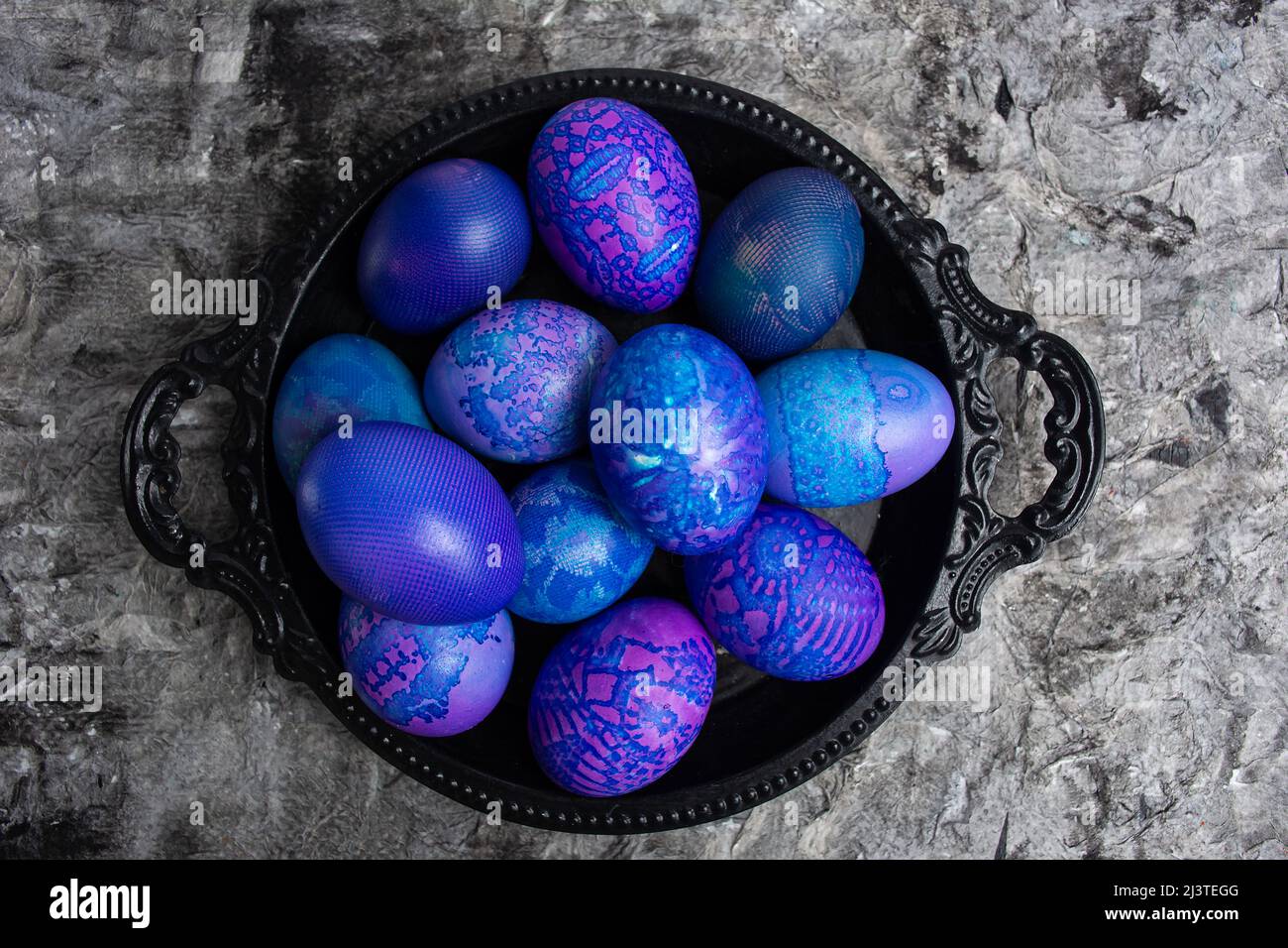 Huevos de Pascua. Huevos de Pascua azul-púrpura pintados en encaje, en un tazón negro sobre un fondo rústico negro, vista superior. Patrón de fondo de huevo. Foto de stock