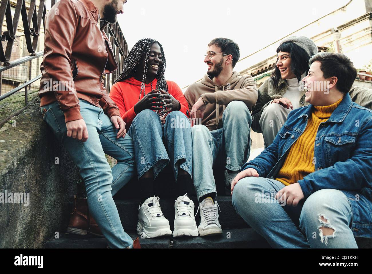 Reunión de compañeros de clase de jóvenes estudiantes multi-culturales sentados en la escalera divirtiéndose charlando juntos Foto de stock
