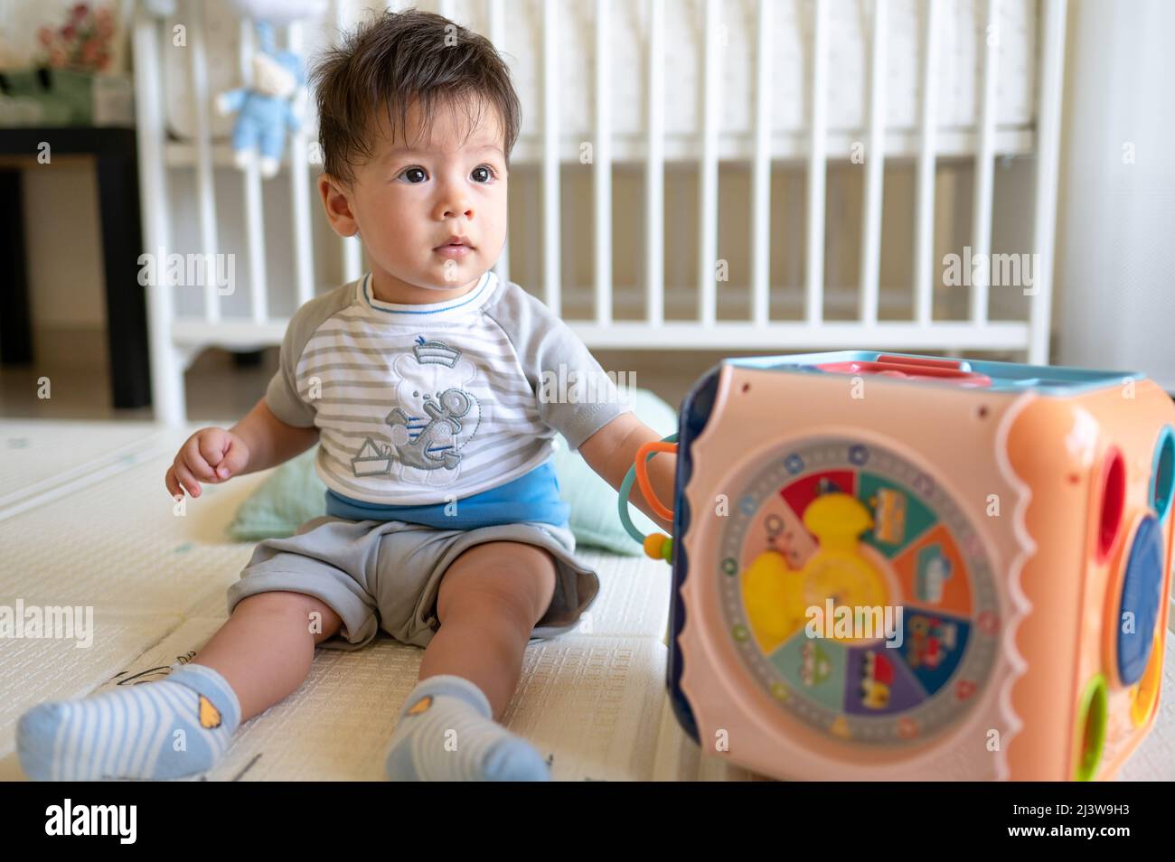 8 meses de edad raza mixta bebé niño jugando con la caja de actividades en el dormitorio mientras está sentado en el suelo cubierto con una alfombrilla de goma Foto de stock
