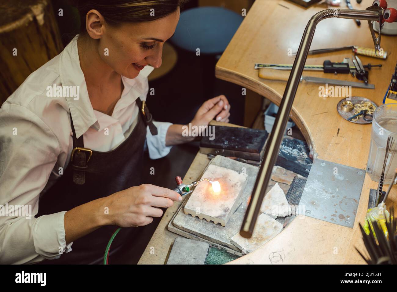 Goldsmith trabajando en un anillo caliente brillante en su banco de trabajo Foto de stock