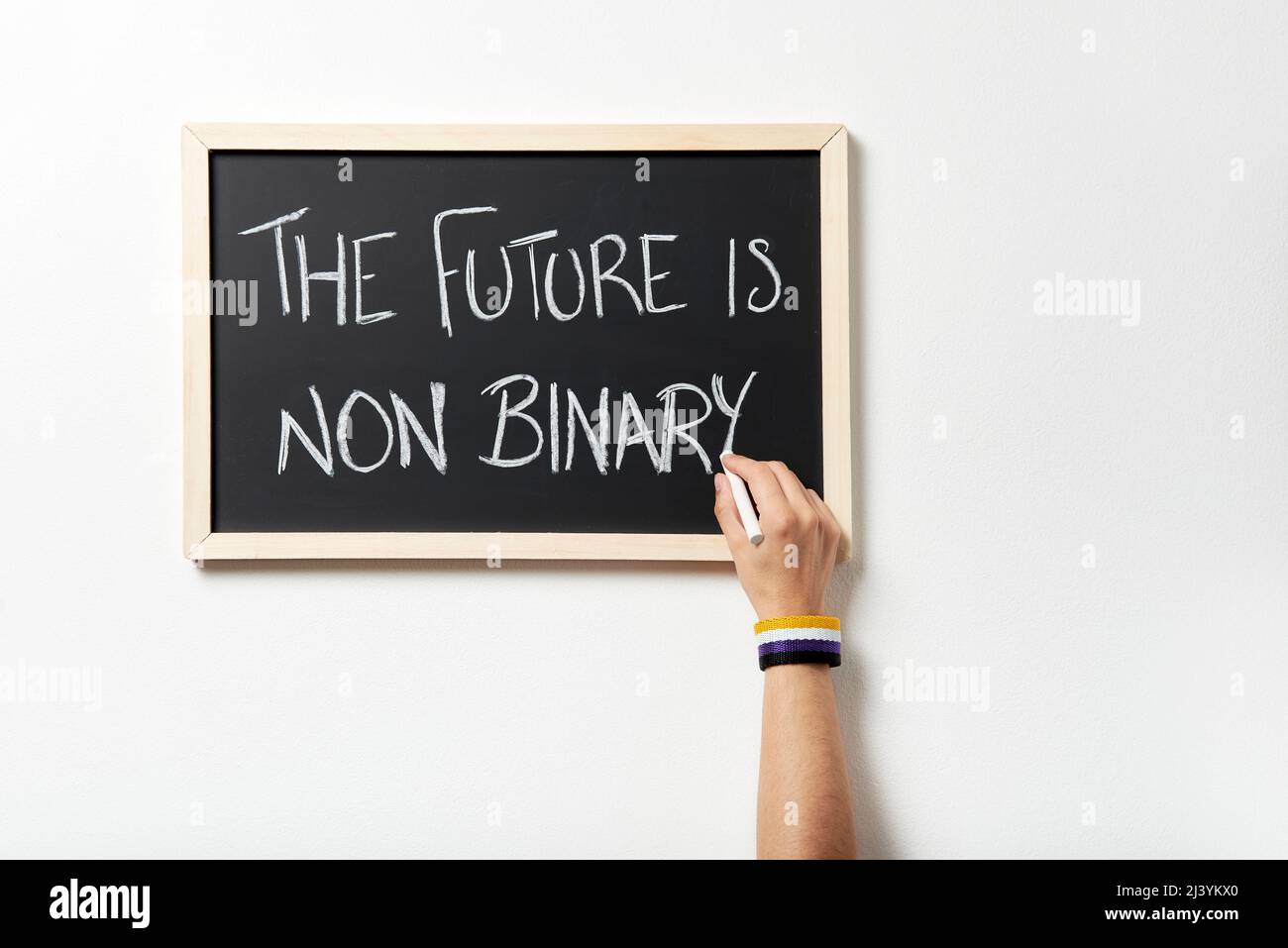 Mano con pulsera simbólica que tiza el texto El futuro no es binario en un pizarrón. Concepto de respeto a la diversidad de género. Foto de stock