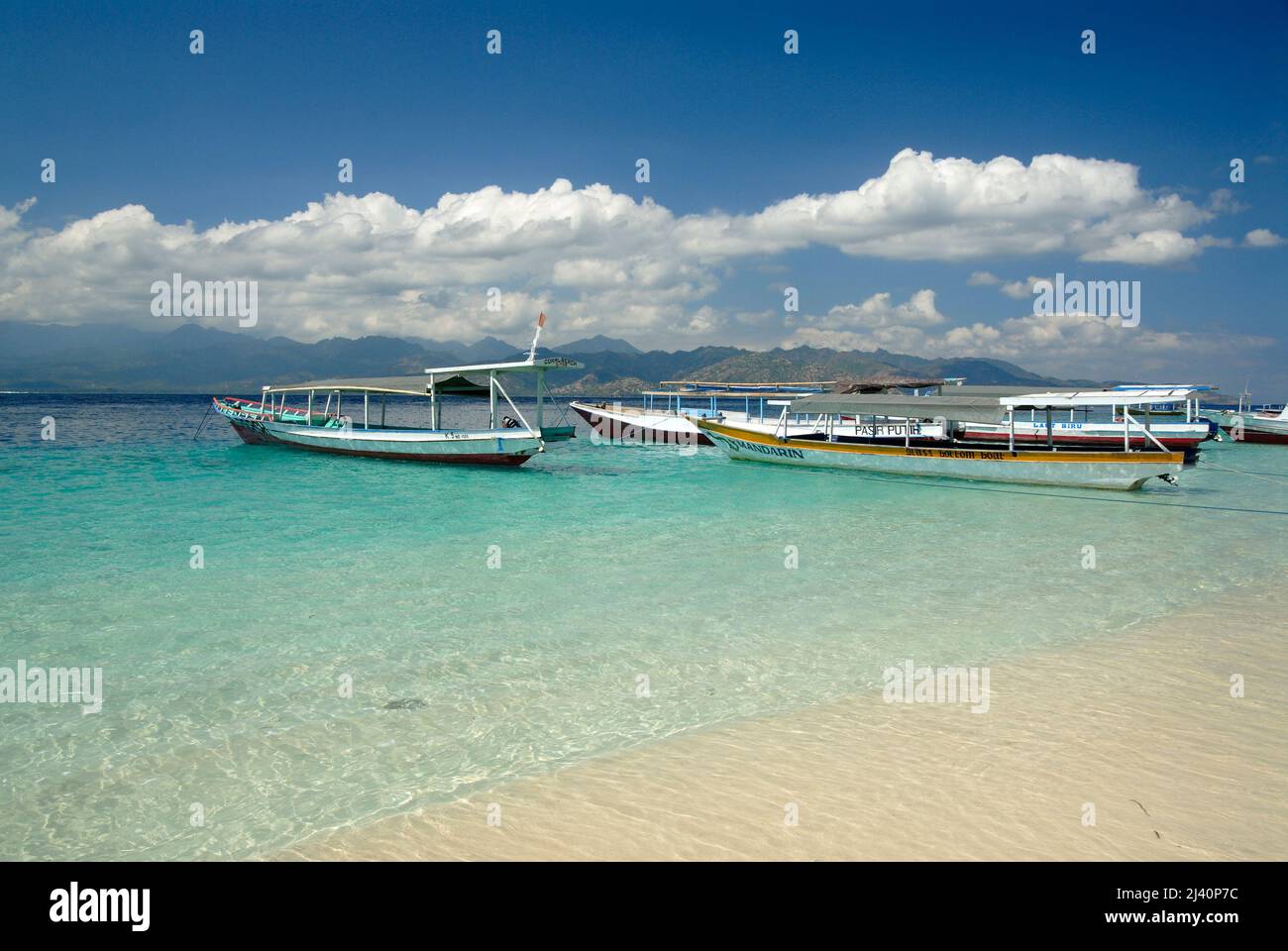 Los barcos utilizados principalmente para transbordar a la gente entre Gili Trawangan y Lombok están amarrados cerca de la playa. Lombok está a la distancia. Foto de stock