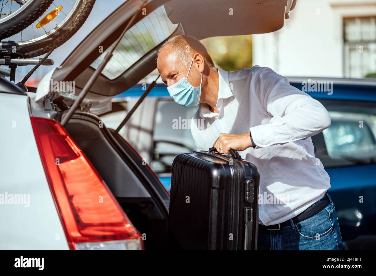 Un taxista o conductor de Uber la máscara pone el equipaje en el maletero de su coche Fotografía de stock - Alamy