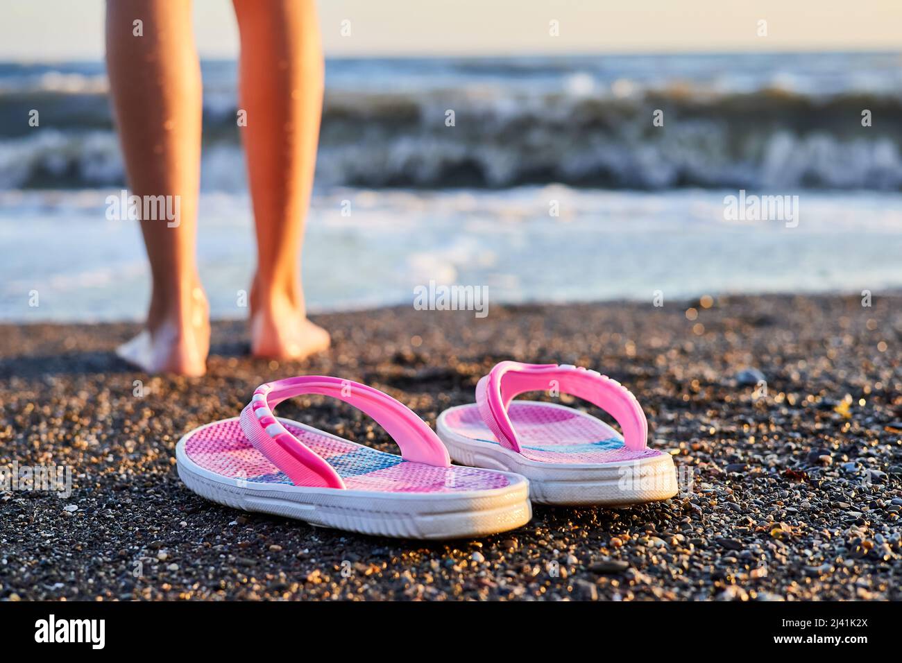 Pantuflas rosadas para niños en una playa de guijarros con patas de niña en  el fondo Fotografía de stock - Alamy