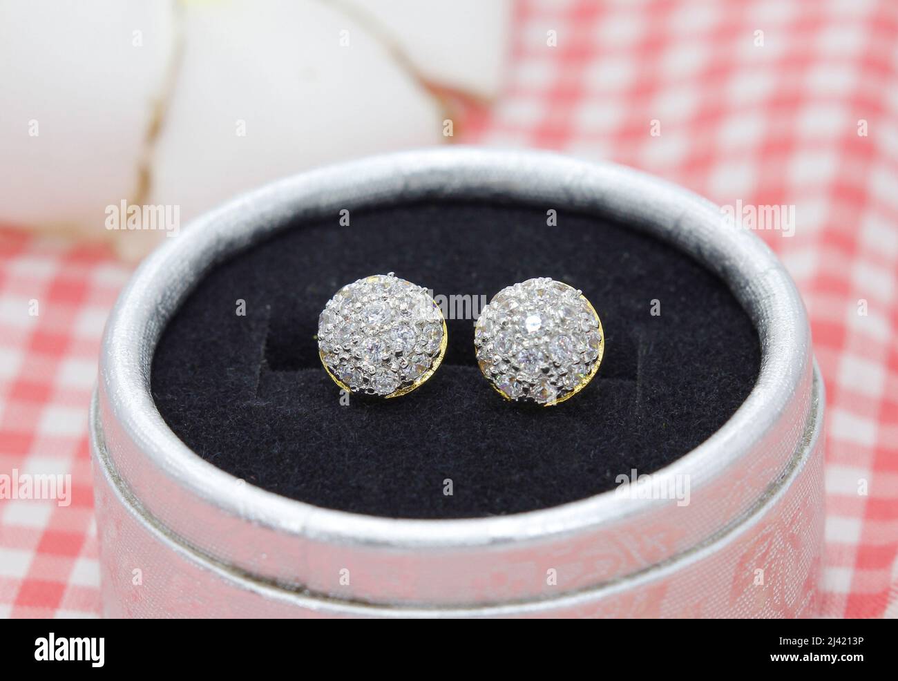 Pendientes dorados de lujo decorados con diamante en caja de joyas sobre fondo de tela de cuadros rojos Foto de stock