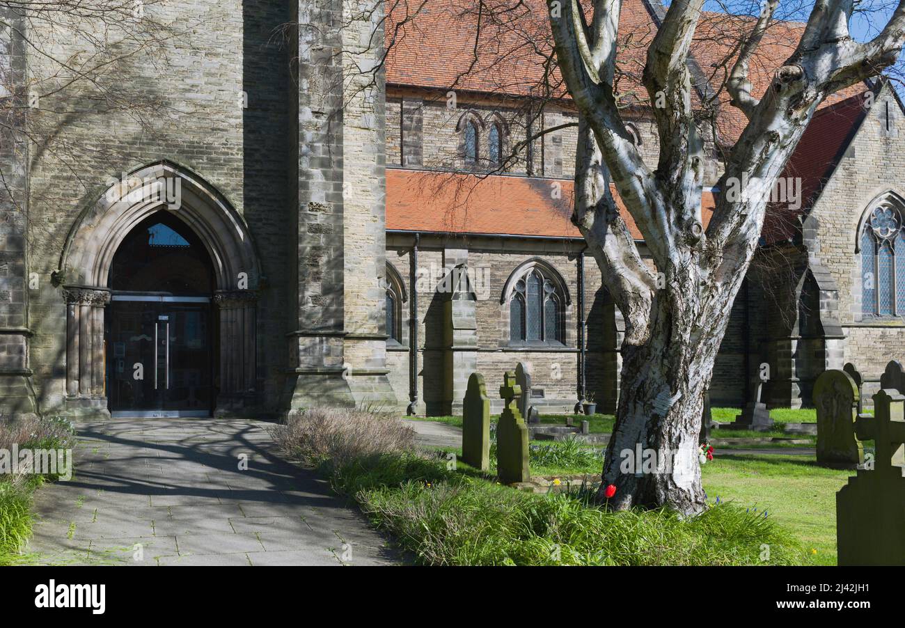 Iglesia de San Nicolás con vista a las lápidas y flanqueada por céspedes y árboles bajo el cielo azul en una fina y soleada morninbg de primavera en Beverley, Yorkshire, Reino Unido. Foto de stock