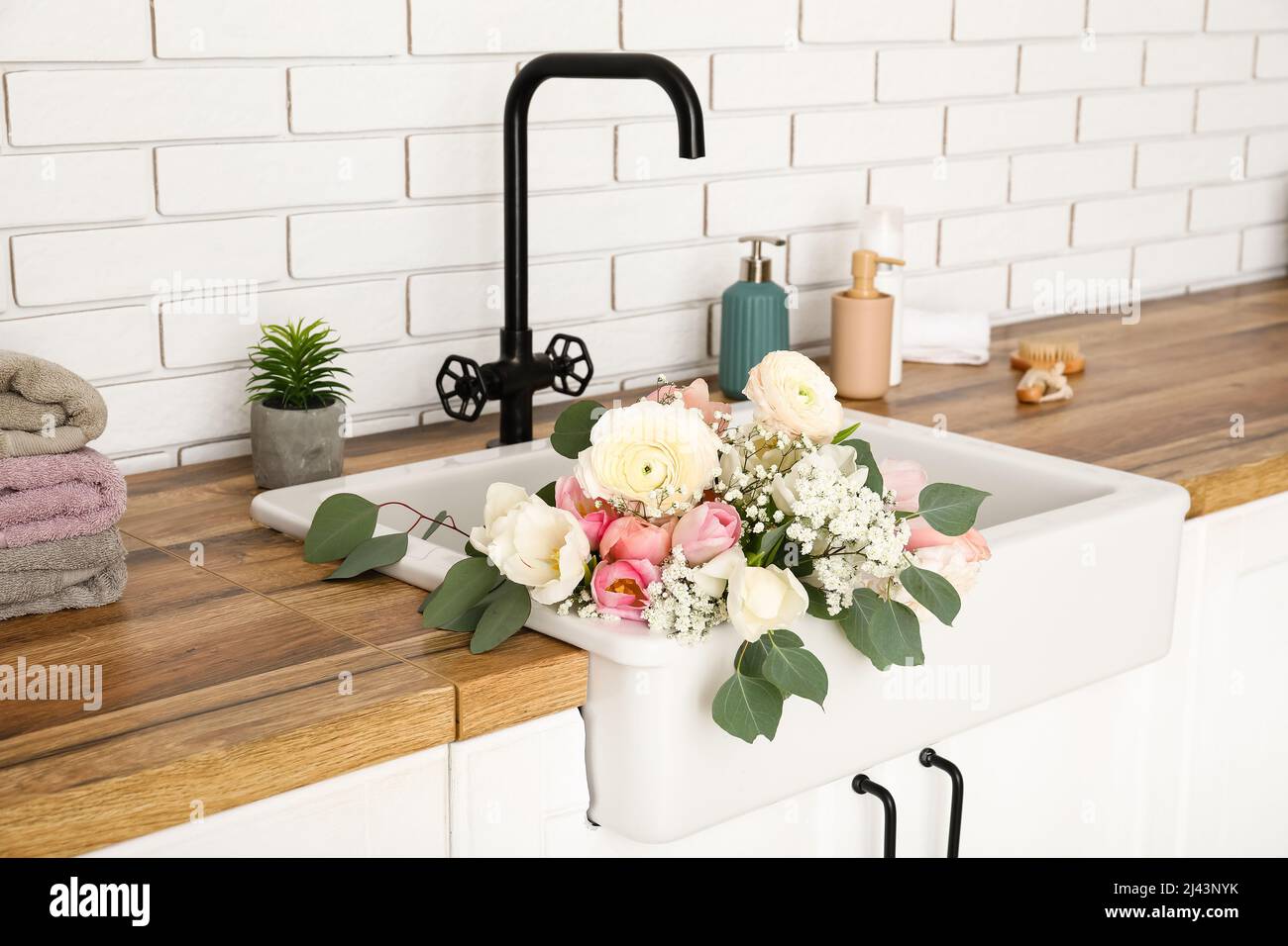 Fregadero con hermosas flores y artículos de baño en mostradores cerca de la  pared de ladrillo blanco Fotografía de stock - Alamy