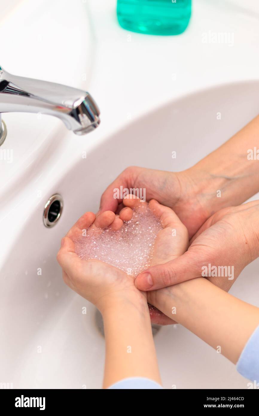 Espuma de jabón en forma de corazón en las manos de los niños sobre el lavabo y las manos de la madre en un baño luminoso. Enfoque selectivo. Primer plano Foto de stock