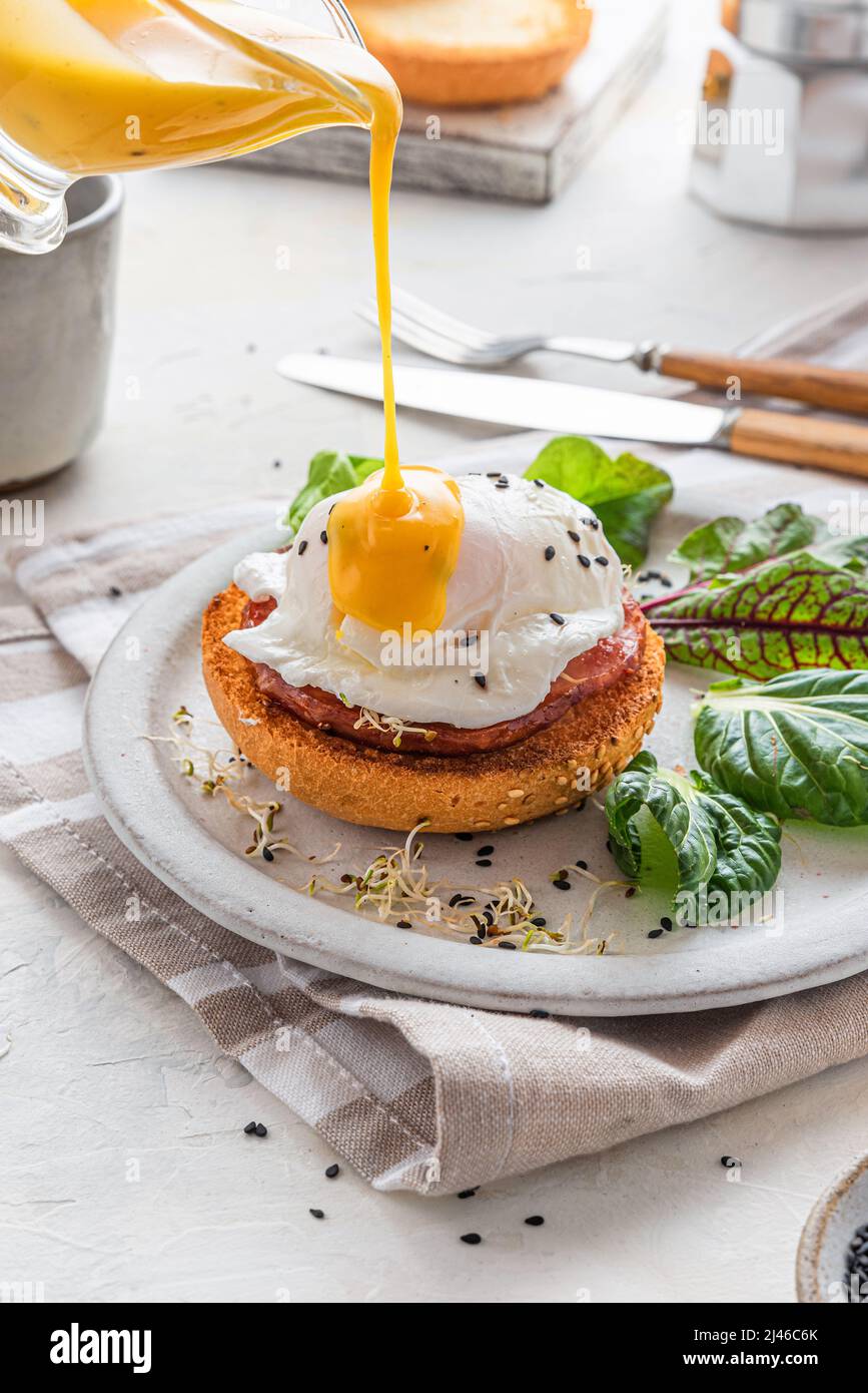 Verter la salsa hollandaise sobre el huevo escalfado para cocinar el huevo benedict para el desayuno sabroso. Orientación vertical. Desayuno-almuerzo inglés Foto de stock