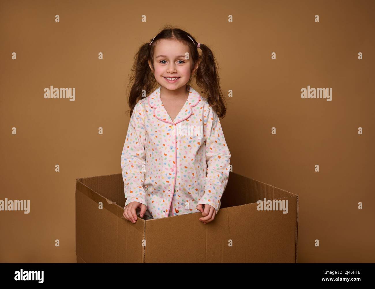 Adorable niño, europea niña de 4 años con dos colas onduladas en un pijama  brillante mirando la cámara de pie dentro de una caja de cartón, aislada  Fotografía de stock - Alamy