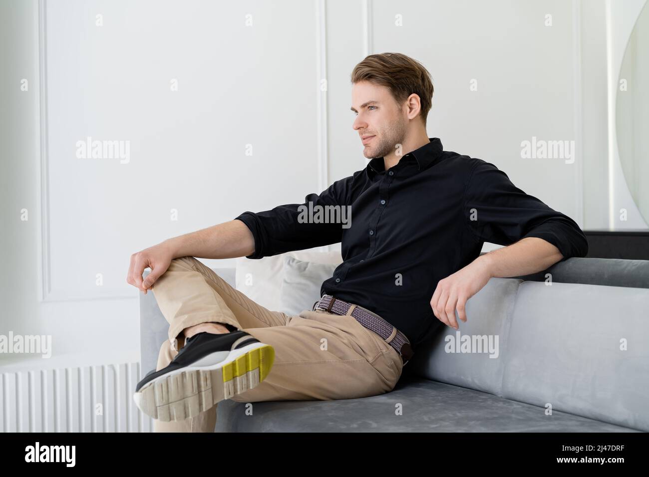 Escribe un reporte métrico anunciar hombre con camisa negra y pantalón beige sentado en el sofá de la sala de  estar Fotografía de stock - Alamy