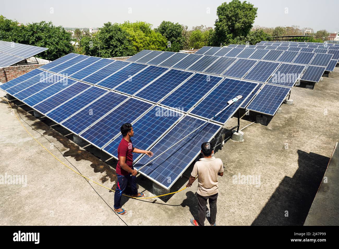 Hombres limpiando paneles solares en el techo del Instituto de Filosofía y Religión Vishwa Jyoti Gurukul de la Sociedad Misionera India IMS en Varanasi, Uttar Pradesh, India Foto de stock