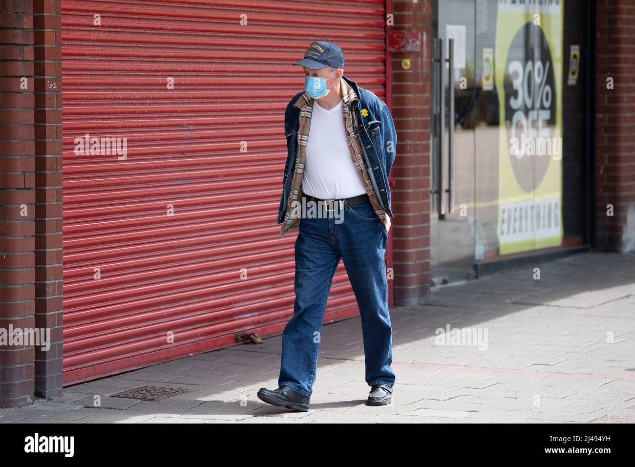Un hombre que lleva una máscara pasa por un pequeño negocio cerrado durante el período de encierro del coronavirus en Barry, Gales, Reino Unido. Foto de stock