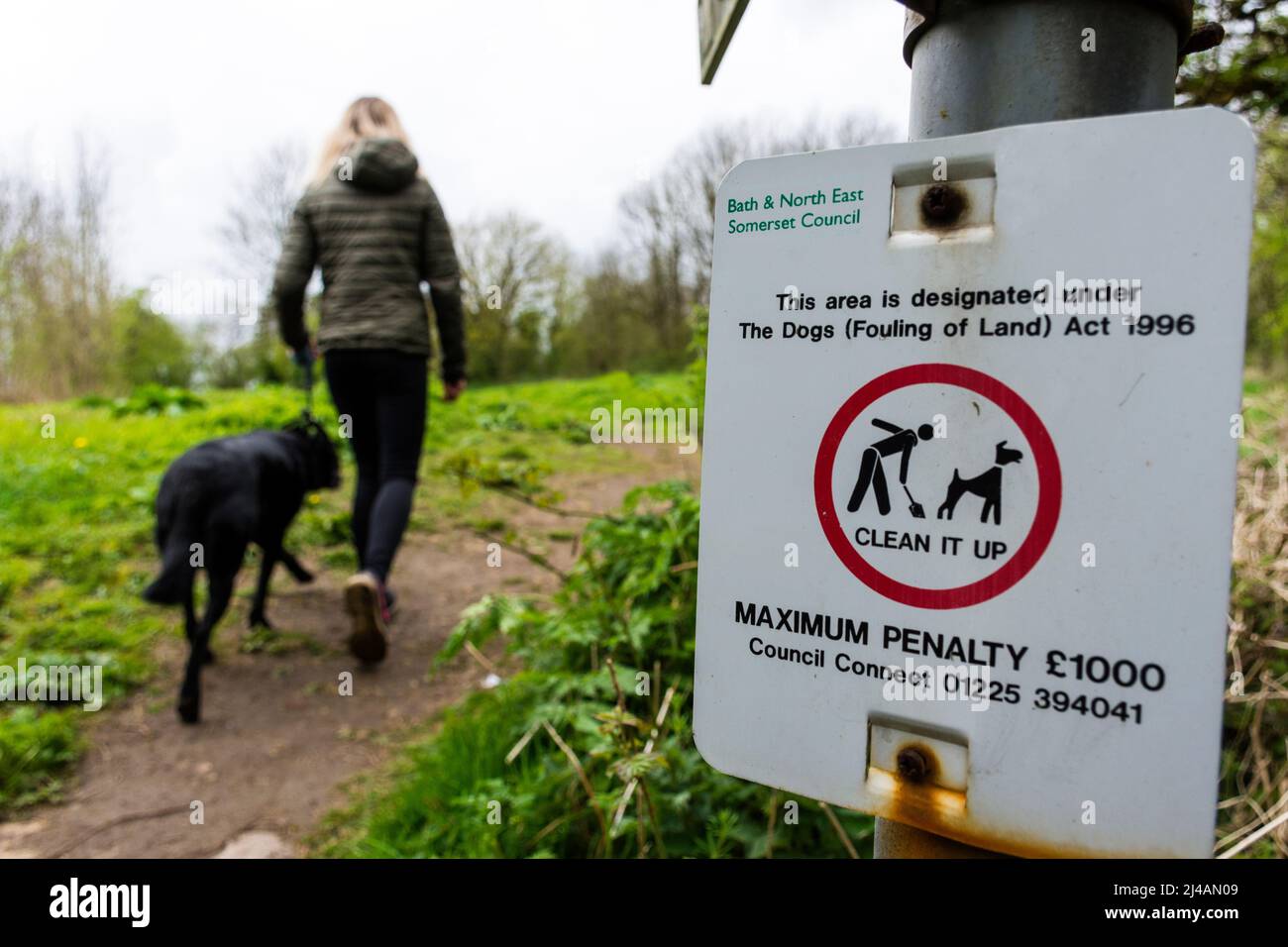 El andador de perros pasa una señal de advertencia que dice de multas por el ensuciamiento de perros en Batheaston, Somerset, Reino Unido Foto de stock