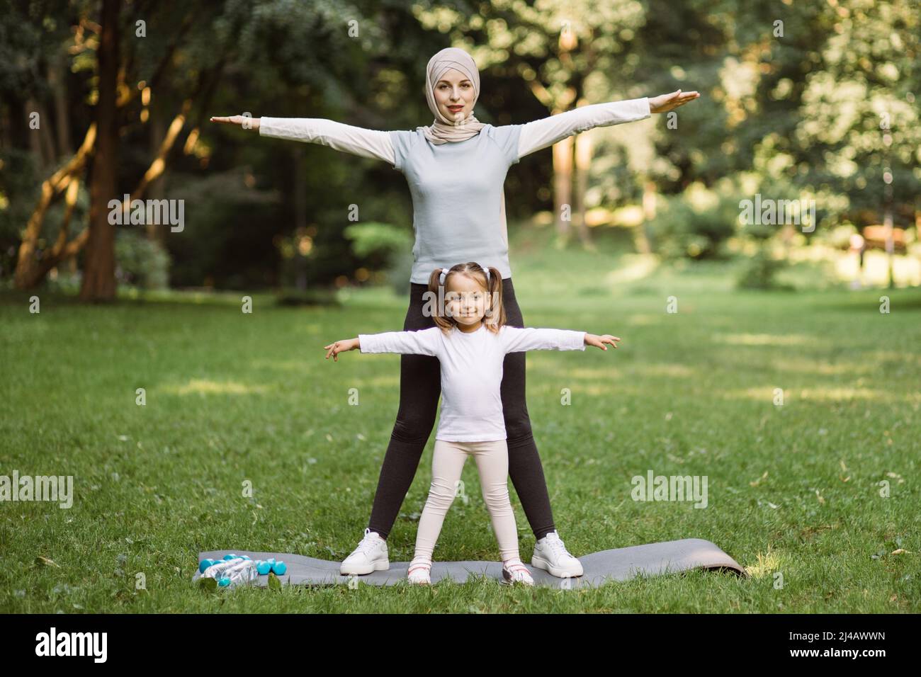 Actividad fitness deportiva familiar. Bonita mujer musulmana en ropa deportiva y hijab y su hija lindo hacer ejercicios deportivos, de pie con brazos extendidos juntos en el de