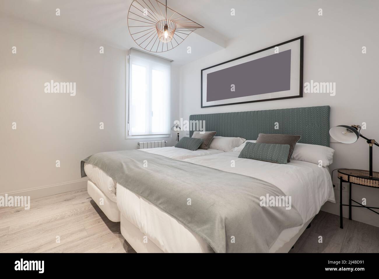 Dormitorio con dos camas individuales juntas, cabecera tapizada en tela  verde, mesitas de noche de mimbre y metal y una hermosa lámpara en el techo  Fotografía de stock - Alamy