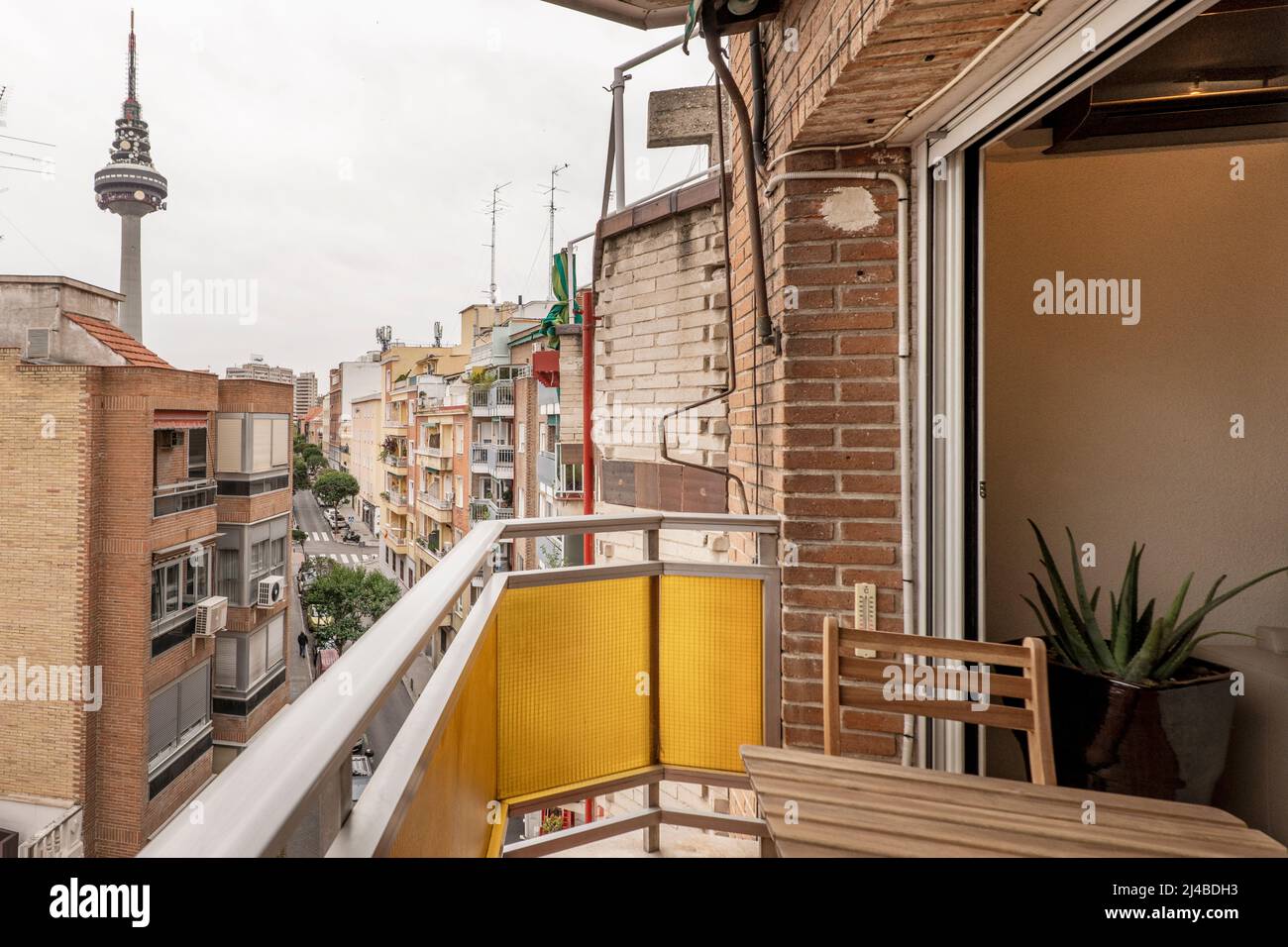 Vistas a algunos edificios y terrazas y a la torre de telecomunicaciones de Madrid desde una pequeña terraza con mesa de teca Foto de stock