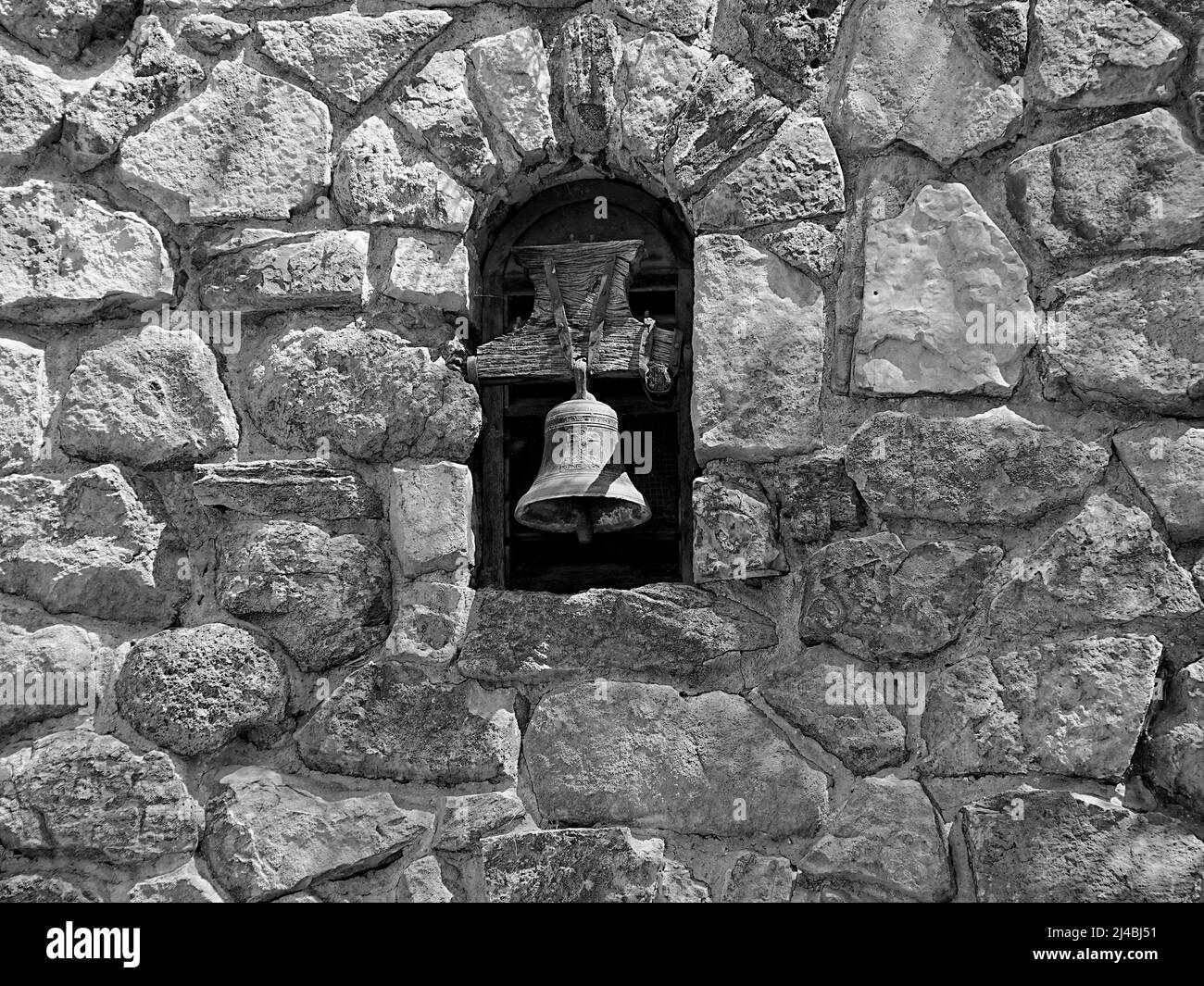 Una campana de estilo misión y el trabajo de piedra que la rodea hacen una interesante fotografía en blanco y negro Foto de stock