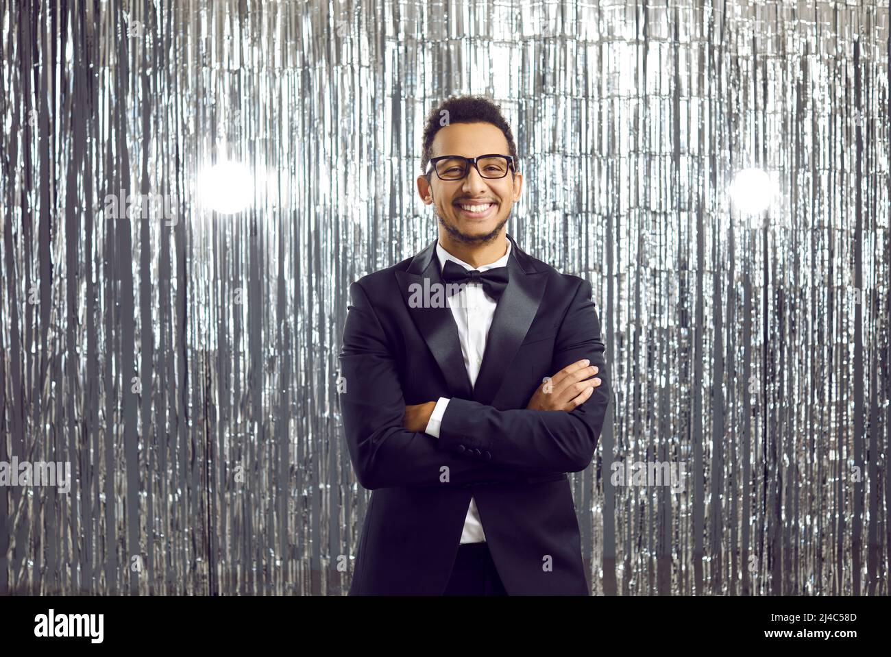 Feliz hermoso caballero negro joven en un elegante tuxedo y gafas en una fiesta Foto de stock