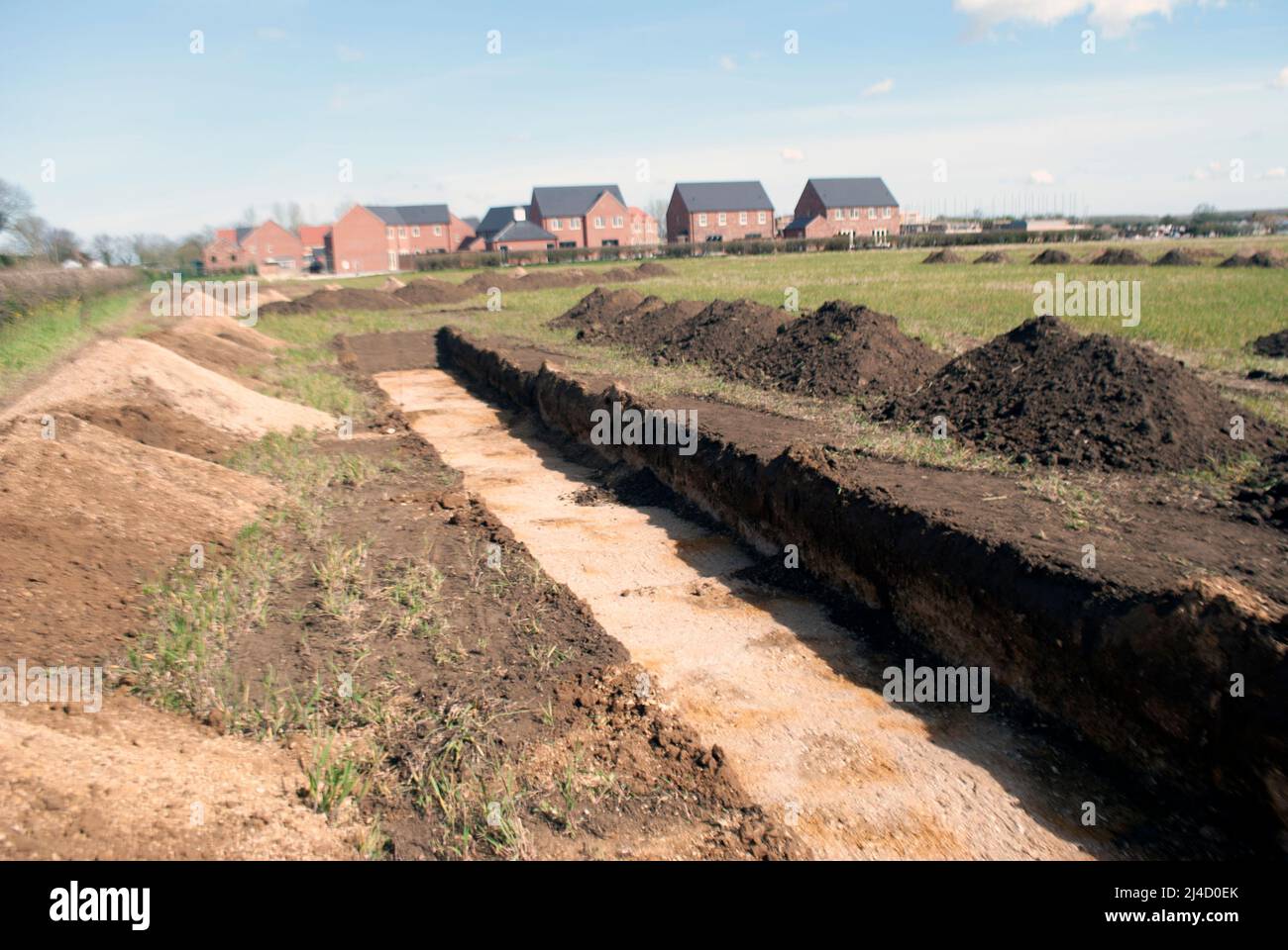 Trincheras excavadas en el campo para el estudio arqueológico con casas de nueva construcción junto al pueblo de Ruskington, Sleaford, Lincolnshire, Inglaterra, Reino Unido Foto de stock