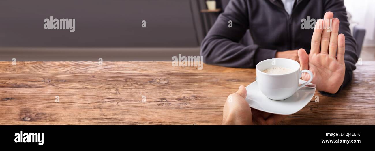 Close-up de una mano de hombre negarse taza de café ofrecido por persona sobre un mostrador de madera Foto de stock