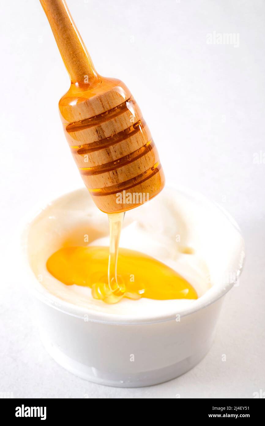 Miel goteando del penetrador en una taza de yogur con fondo blanco aislado Foto de stock